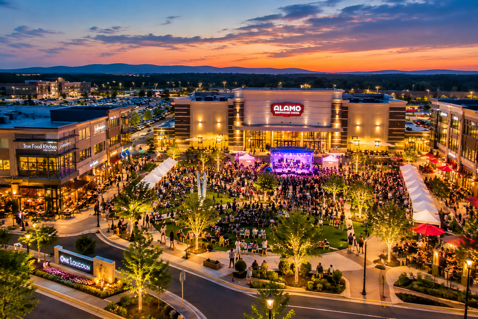 Evening aerial view of the One Loudoun town center green with a crowd gathered for an outdoor concert