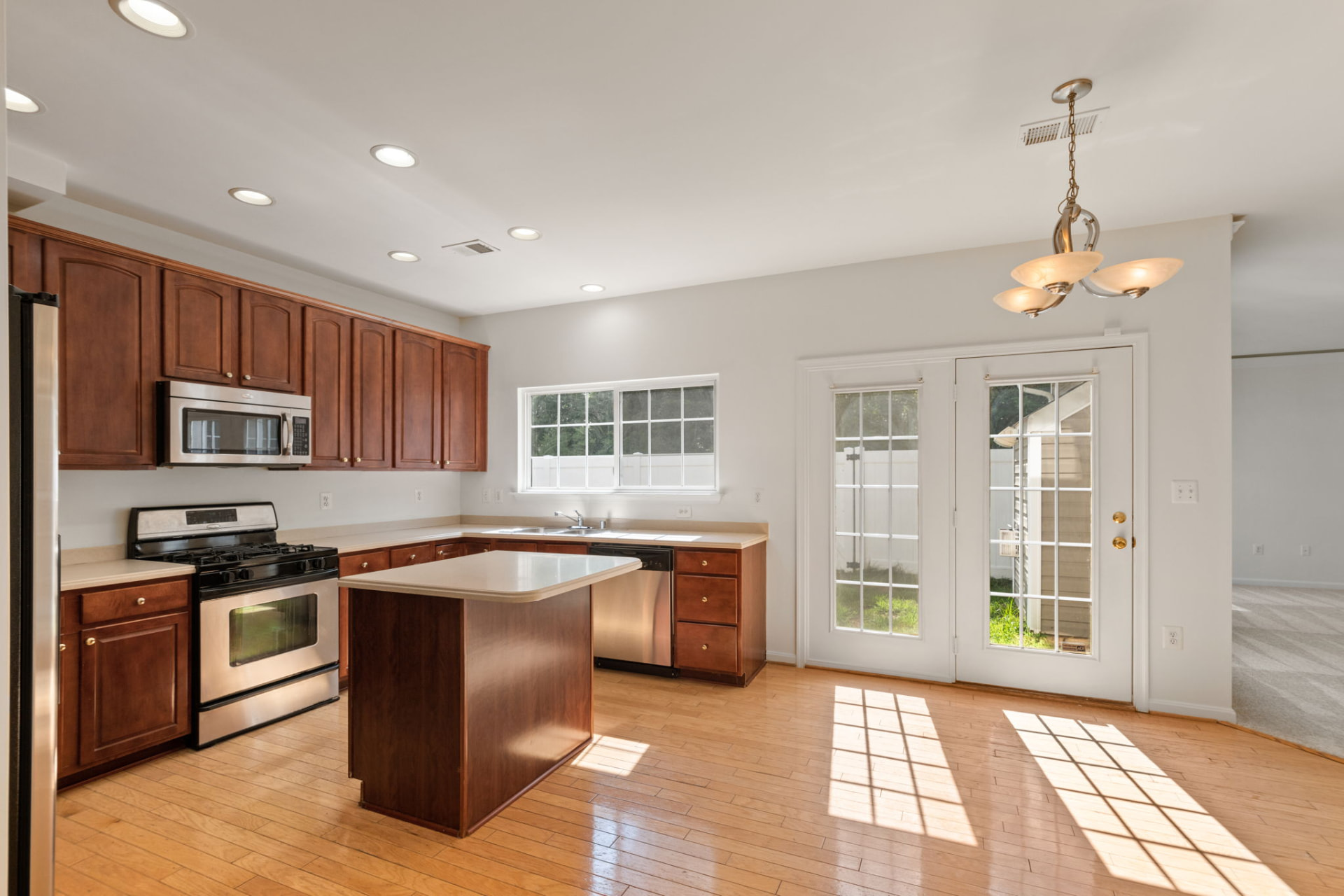 Kitchen of a managed rental home with cherry cabinets, an island, hardwood floors, and French doors to the yard