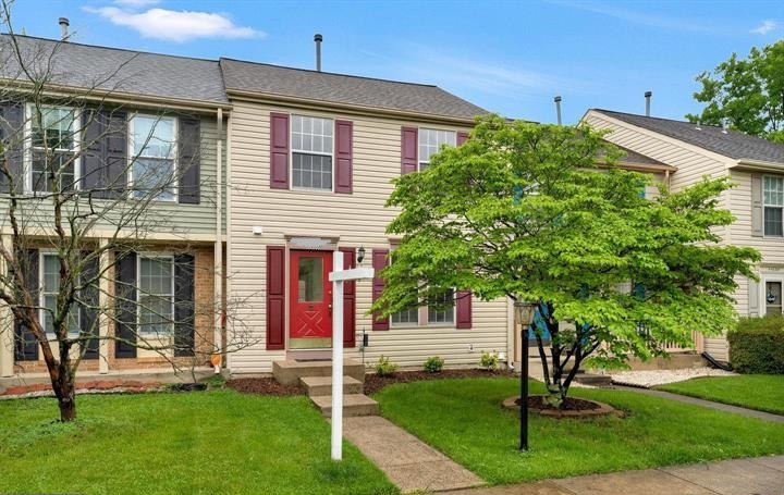 Front exterior of a managed townhouse with a red front door, shutters, walkway, and a small tree on the lawn