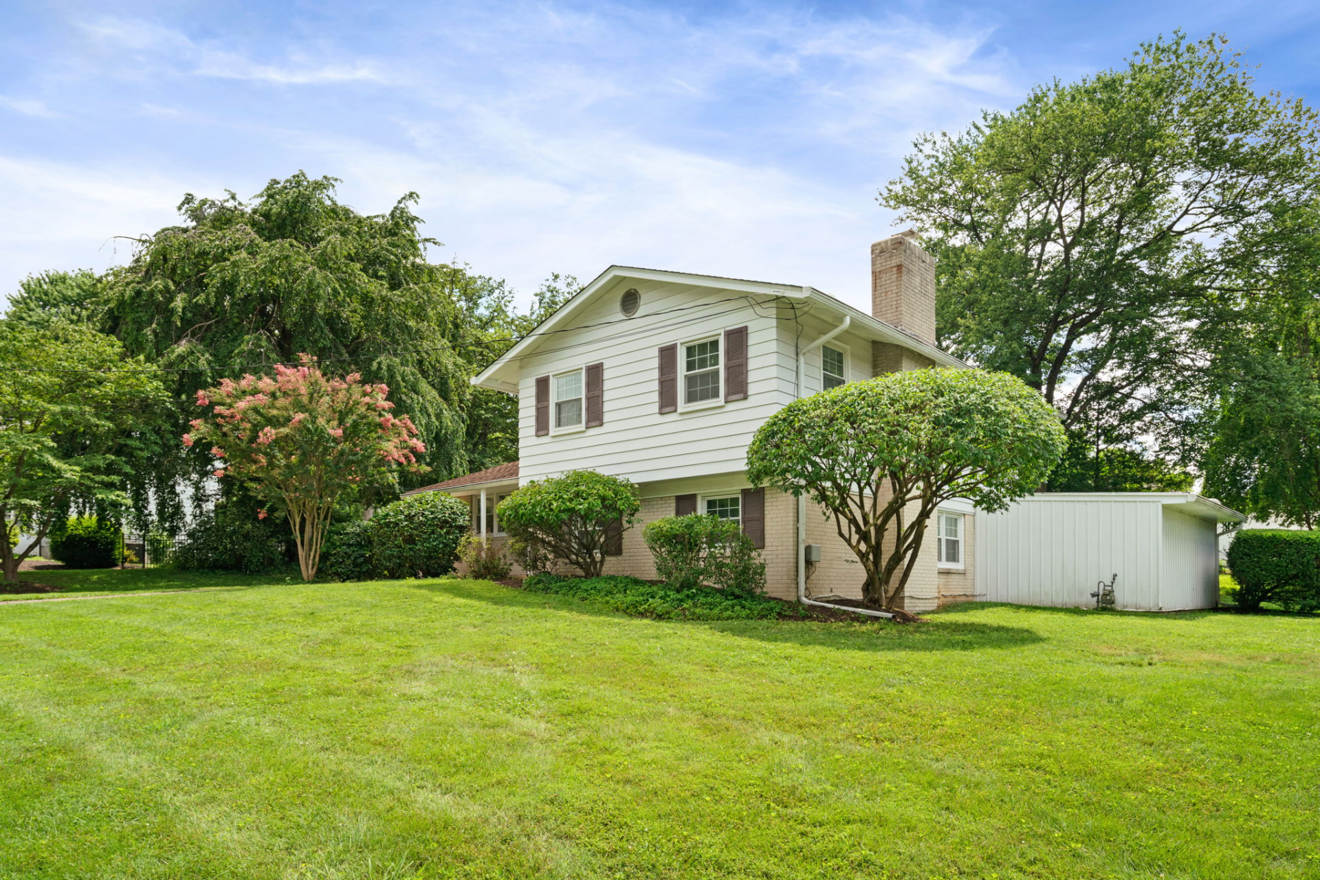 Managed single-family home with light siding and brick, flowering shrubs, mature trees, and a wide lawn