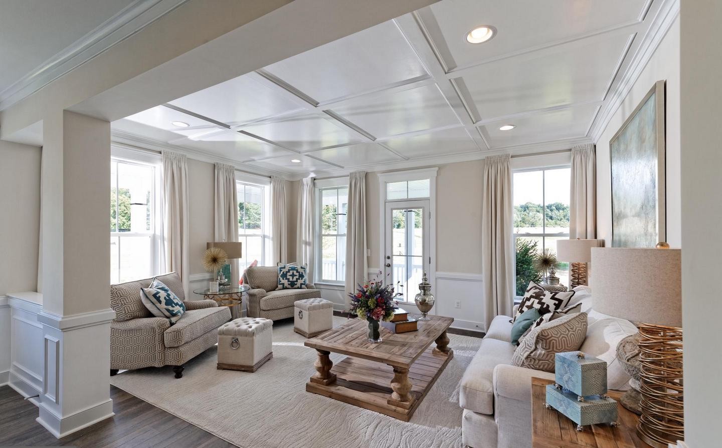 Staged living room with coffered ceiling, neutral sofas, tall windows, and a wood coffee table